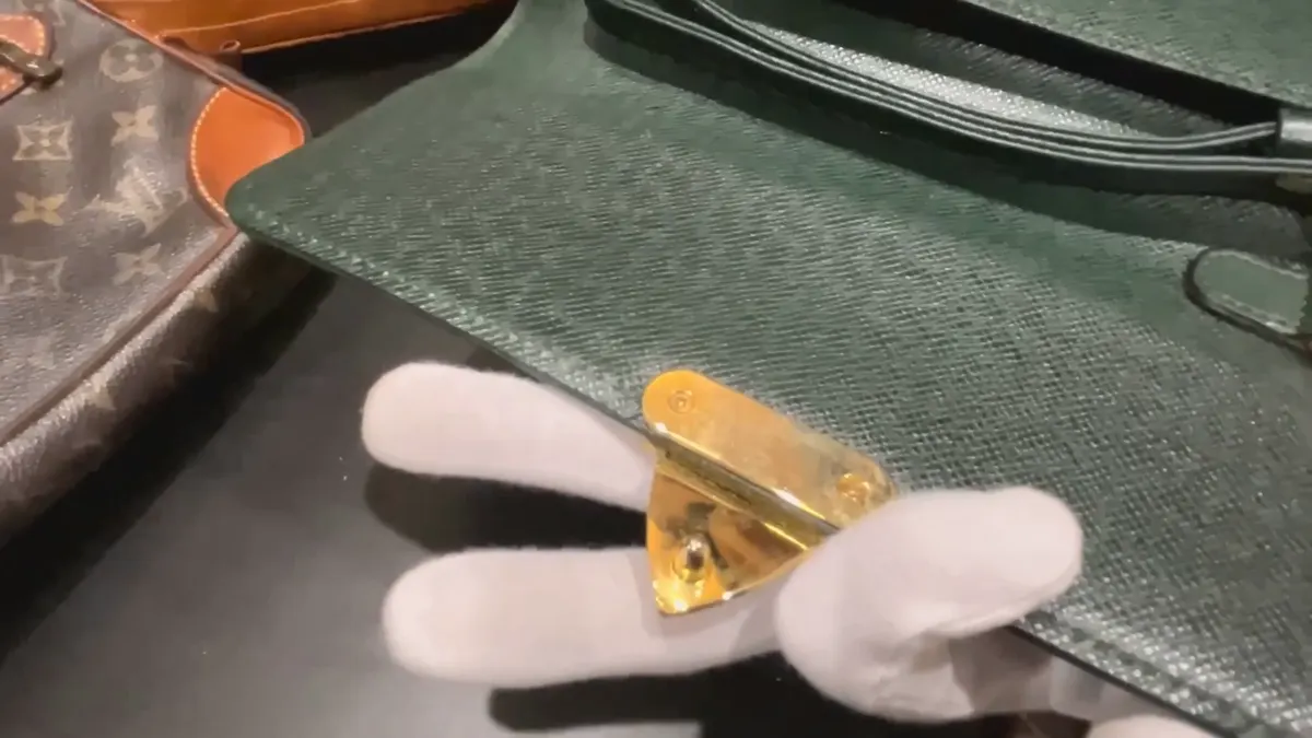 偽物と判定したタイガのセカンドバッグのフラップの金具を手に取って見ているところ